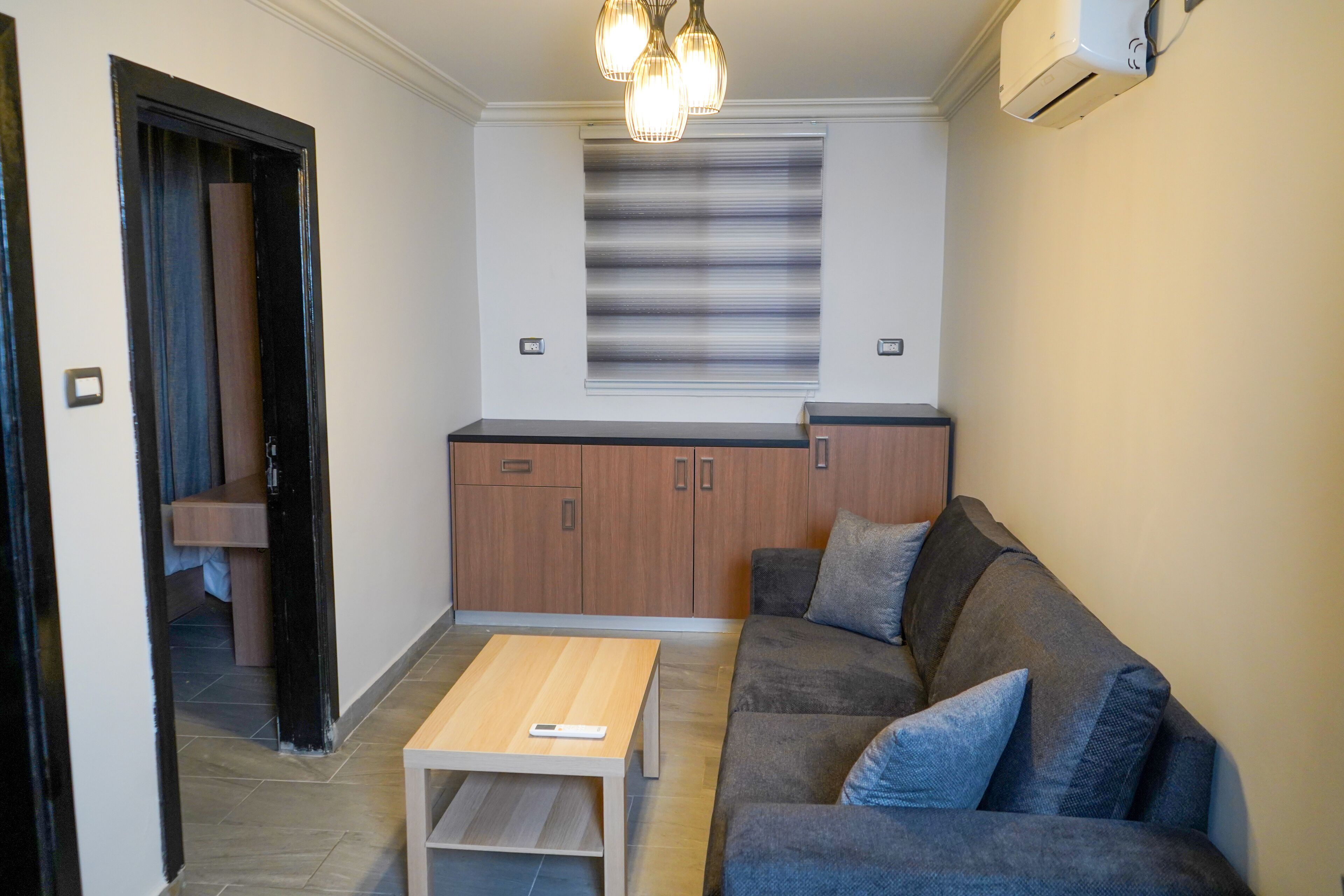 A compact living space with a sofa, a coffee table, a kitchen area with cabinets, and a window with blinds.