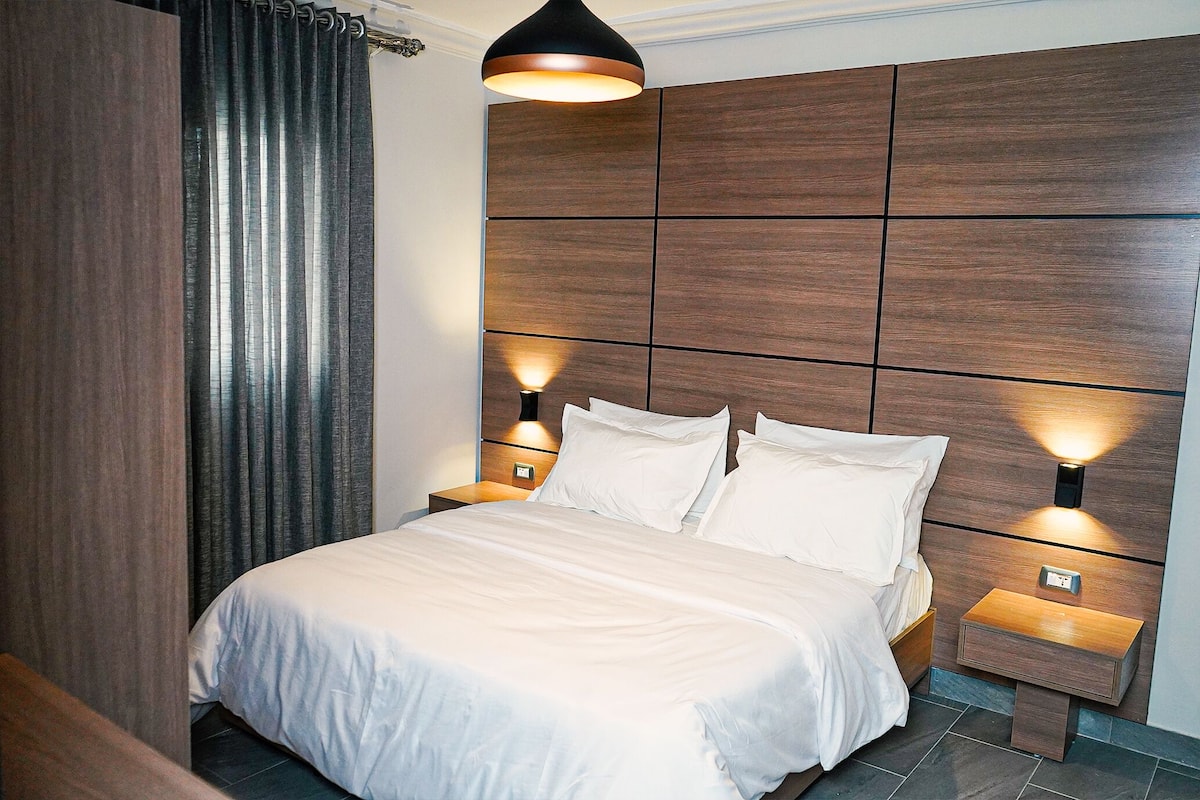 Una habitación de hotel moderna con una cama grande, dos mesitas de noche y un cabecero de madera.