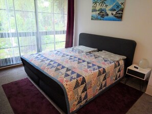Ein Schlafzimmer mit einem großen Bett, einem Nachttisch, einer Wanduhr und einem Bild mit einer tropischen Szene.