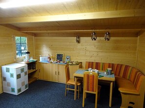 Ein gemütliches Holzinterieur mit Esstisch, Stühlen, einer Bank, einem Kühlschrank und einem Fenster.