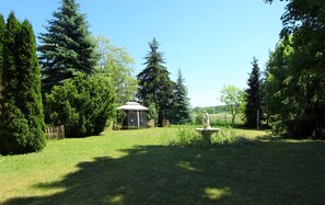 Ein gepflegter Garten mit einem Pavillon, einer Statue und verschiedenen Bäumen.
