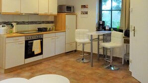 Eine moderne Küche mit weißen Schränken, einer Mikrowelle und einem Herd. Ein Essbereich mit zwei weißen Tischen und Stühlen ist ebenfalls vorhanden.
