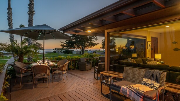 An outdoor patio with wooden flooring, wicker furniture, and a glass-enclosed living area with a view of the ocean. - Bluewater Retreat - Ocean Views from the heart of Santa Barbara (Santa Barbara)