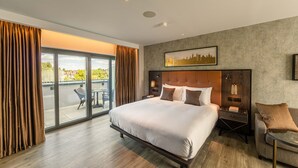 A modern hotel room with a large bed, a nightstand, a chair, and a balcony with a table and chairs. - The Fellows House Mews (Cambridge)