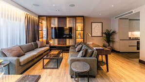 A modern living room with a sofa, a coffee table, a TV, and a dining area. - The Fellows House Mews (Cambridge)