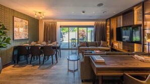 A modern living room with a dining area, a sofa set, a TV, and a large window with curtains. - The Fellows House Mews (Cambridge)