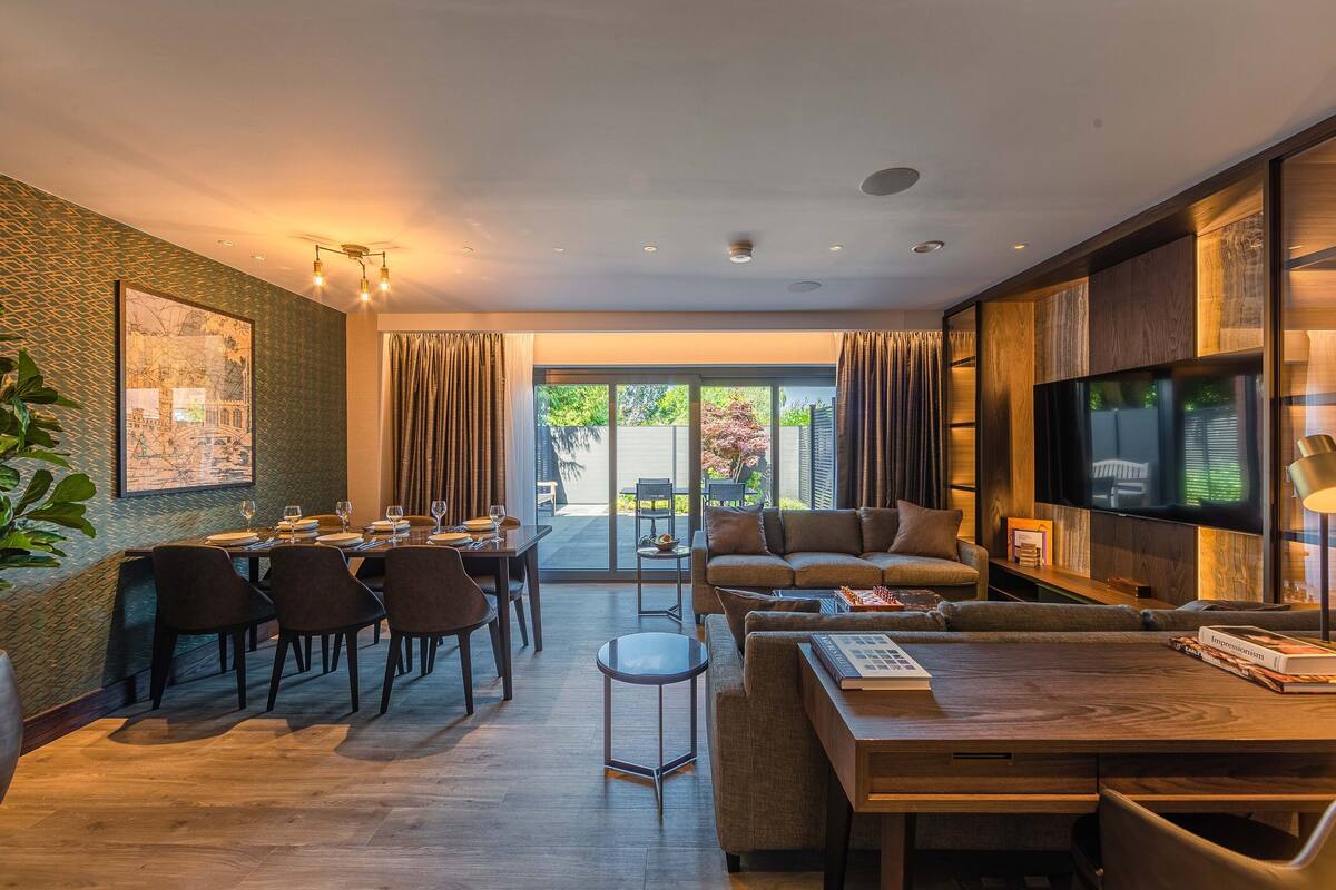Uma sala moderna com área de jantar, um conjunto de sofá, televisão e uma janela grande com cortinas.