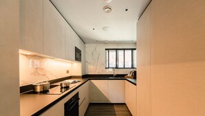 A modern kitchen with white cabinets, a black countertop, and a wooden floor. - The Fellows House Mews (Cambridge)