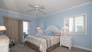 Een slaapkamer met een bed, nachtkastjes, een dressoir, een plafondventilator en een raam met jaloezieën.