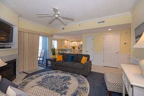 A living room with a fireplace, a ceiling fan, a sofa with cushions, and a dining area in the background. - Luxury 5 Bedroom, 5 Bathroom mobility friendly, double condo with an outdoor rooftop pool, stylish decor  and free WiFi. Linens are included with this property. Just a Few Steps to the Beach! (Ocean City)