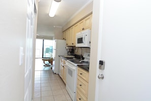 A kitchen with white appliances, wooden cabinets, and a tiled floor.
