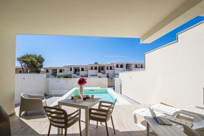 A poolside area with a table, chairs, and a laptop.
