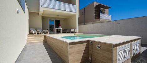 A modern two-story building with a swimming pool, outdoor seating, and a covered area.
