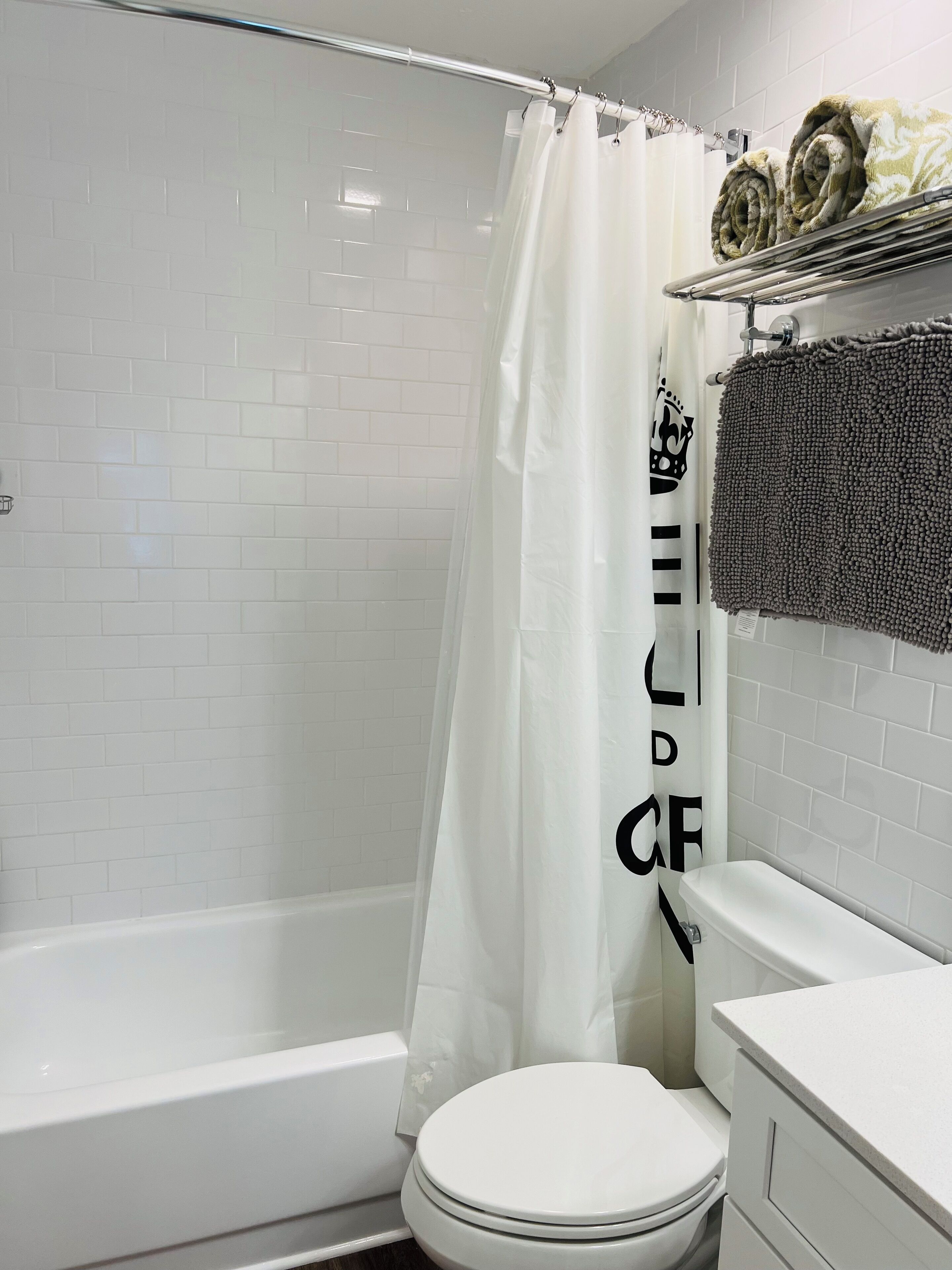 Un baño con ducha de azulejos blancos, un inodoro blanco y un lavabo con un perchero encima.