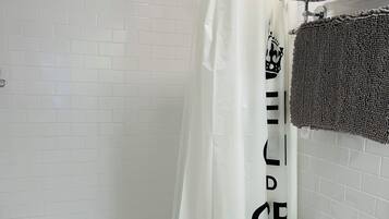Un baño con ducha de azulejos blancos, un inodoro blanco y un lavabo con un perchero encima.