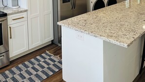 A modern kitchen with white cabinets, stainless steel appliances, a granite countertop, and pendant lighting.