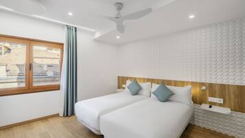 Une chambre d’hôtel moderne avec deux lits, un ventilateur de plafond, une grande fenêtre avec des rideaux et un mur à texture.