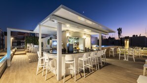 Un área de bar al aire libre con taburetes blancos y una barra, rodeada por una terraza de madera.