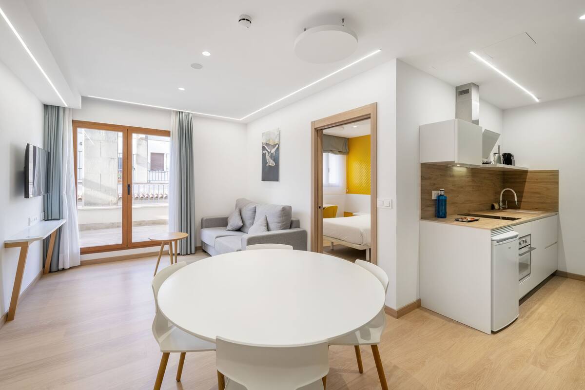 Eine moderne Wohnung mit Essbereich, einer Küchenzeile, einem Wohnzimmer mit Sofa und einem Balkon.