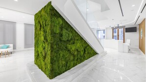 Un vestíbulo moderno con un jardín vertical verde, un mostrador de recepción y una escalera blanca.