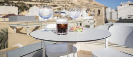 A table with two glasses of water and a glass of cola on a rooftop terrace with a mountain view.