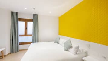 Een moderne hotelkamer met een groot bed, een nachtkastje, een raam met gordijnen en een heldergele accentmuur.
