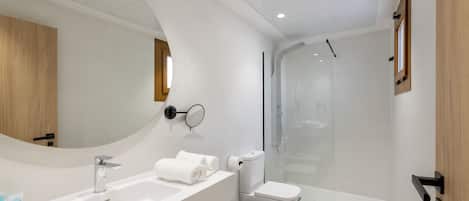 A modern bathroom with a large mirror, a sink, a toilet, and a glass-enclosed shower.