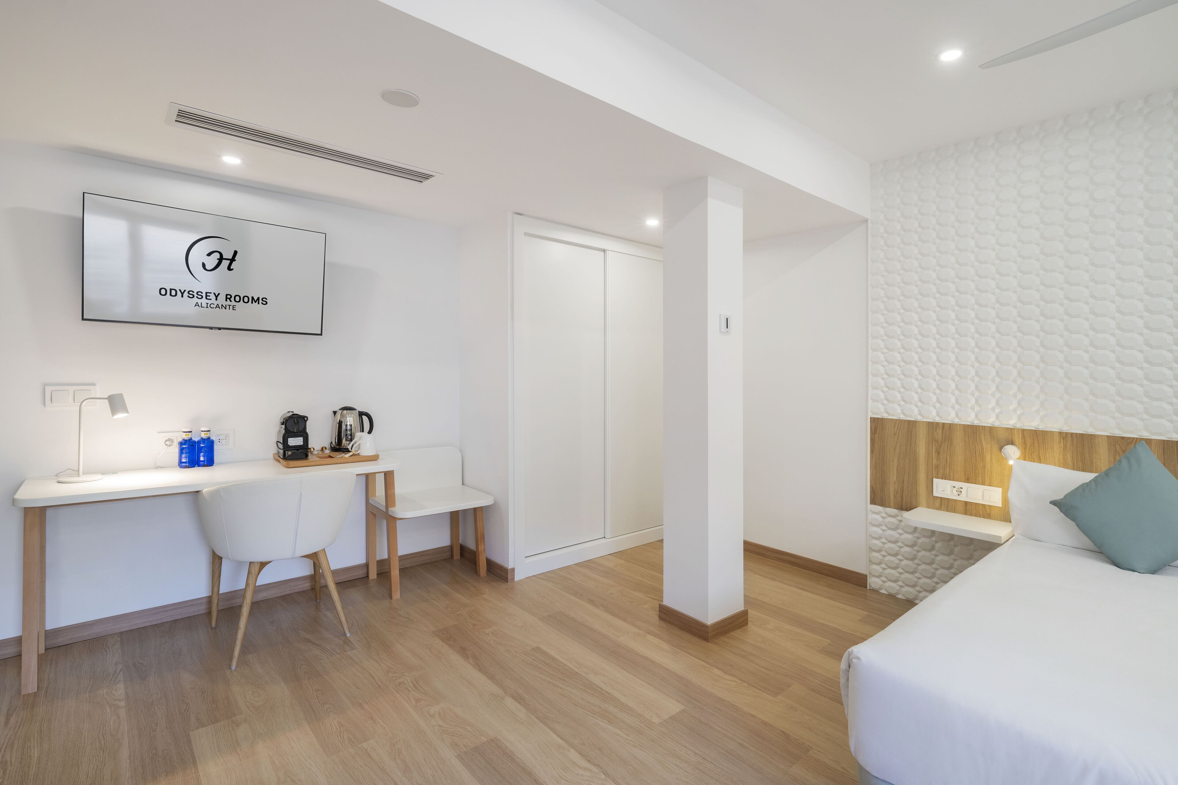 A modern hotel room with a bed, a desk with a chair, a coffee maker, and a TV mounted on the wall.