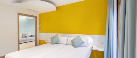 A modern hotel room with a large bed, a bedside table, and a view of a hallway with a sofa.