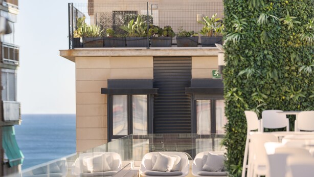 Una terraza en la azotea con sillas blancas, una barandilla de vidrio y vistas al mar.