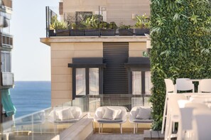 Una terraza en la azotea con sillas blancas, una barandilla de vidrio y vistas al mar.