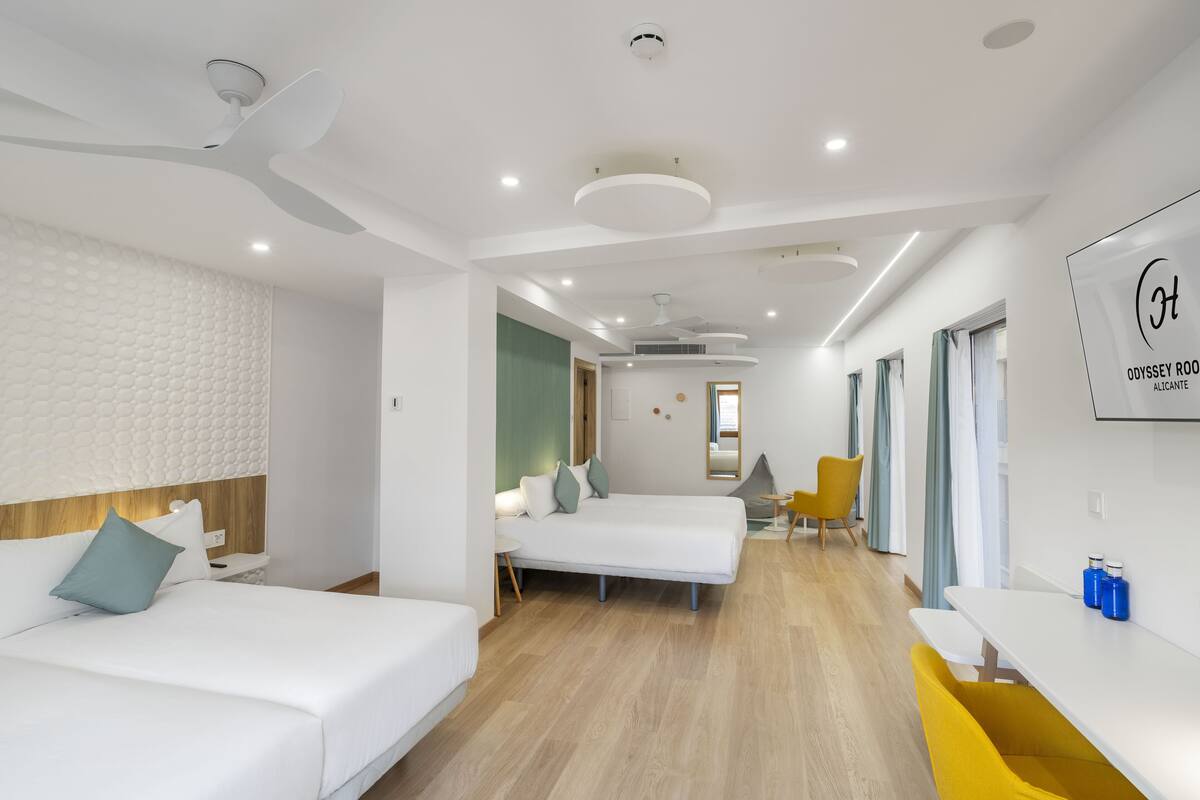 Ein modernes Hotelzimmer mit zwei Einzelbetten, einem kleinen Tisch, einem Sessel und einem Schreibtisch mit Stuhl.