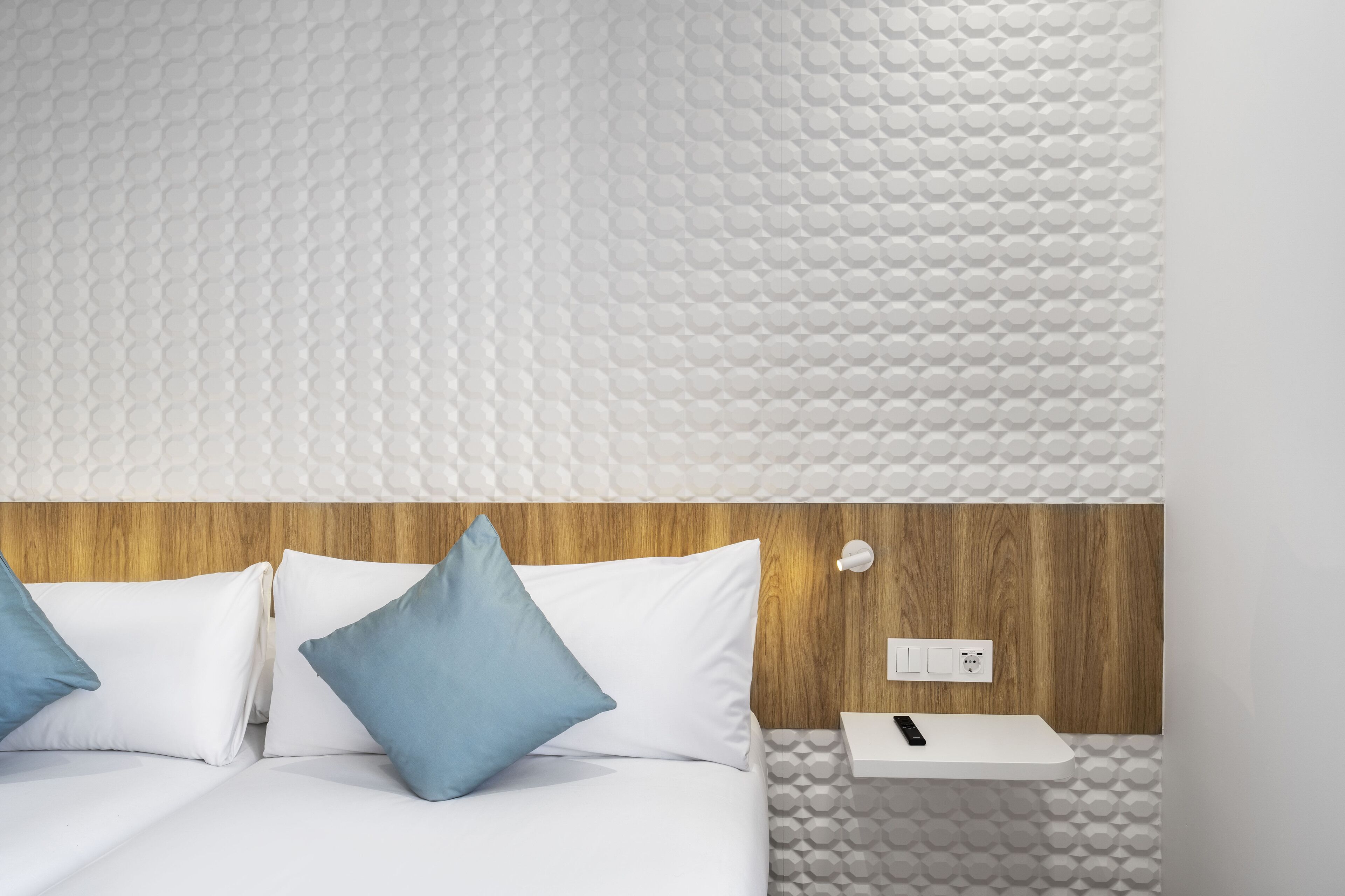 Una habitación de hotel moderna con cabecera de madera, ropa de cama blanca y un diseño de pared con estampado geométrico.