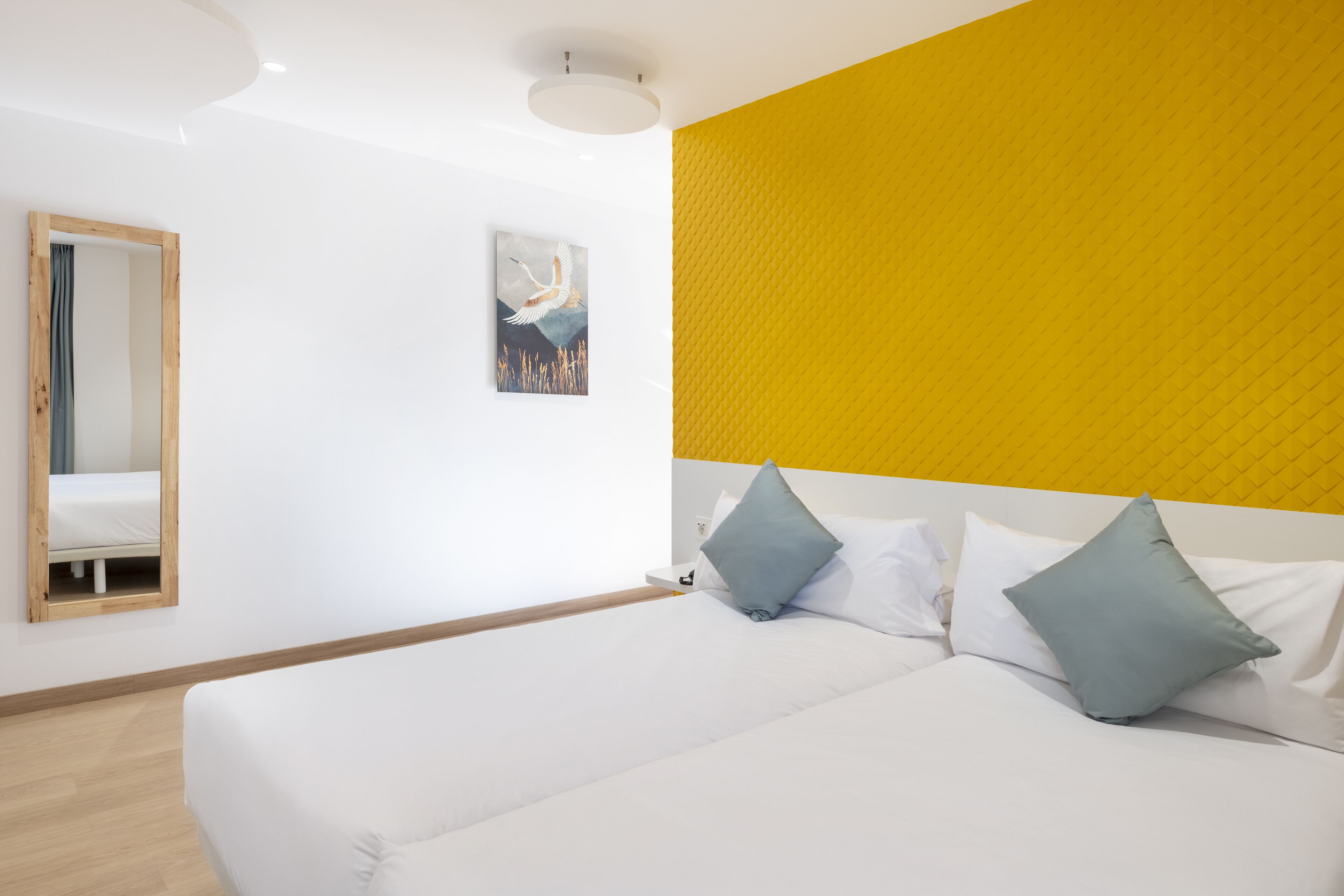 A modern hotel room with a large bed, a mirror, and a yellow accent wall.