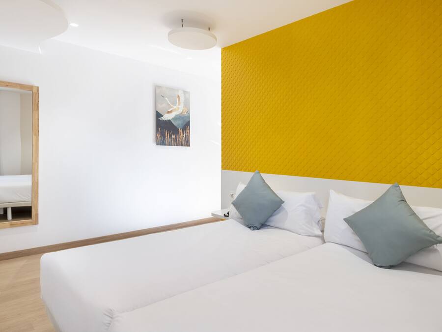 Una habitación de hotel moderna con una cama grande, un espejo y una pared de acento amarilla.