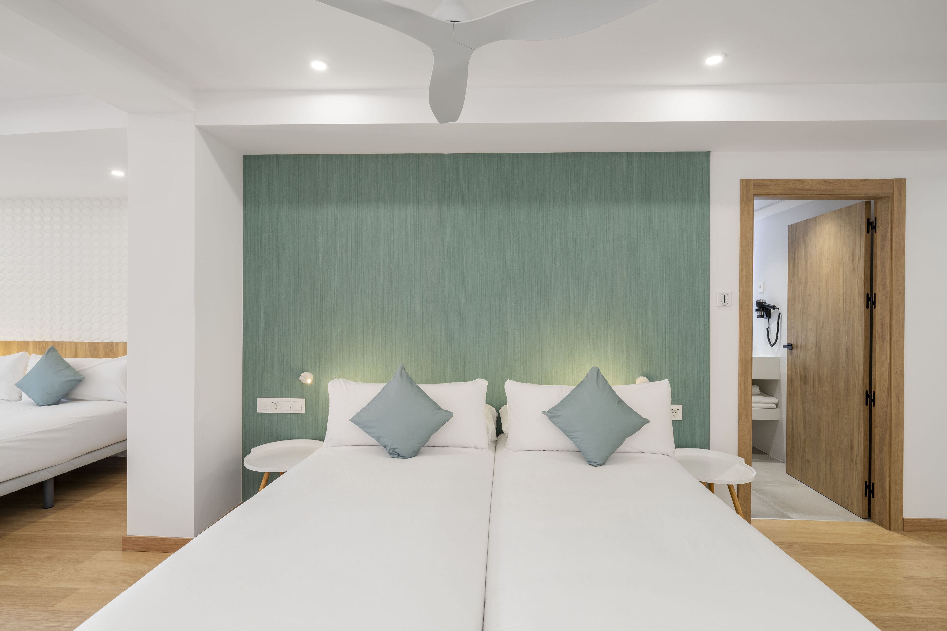 Una moderna camera d'albergo con un letto grande, due comodini, una parete verde decorativa e una porta in legno che dà sul bagno.