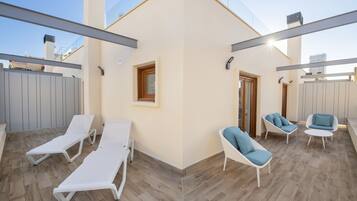 Un patio exterior con sillones blancos y sillas con cojines azules, una puerta de madera y vistas del horizonte de la ciudad.