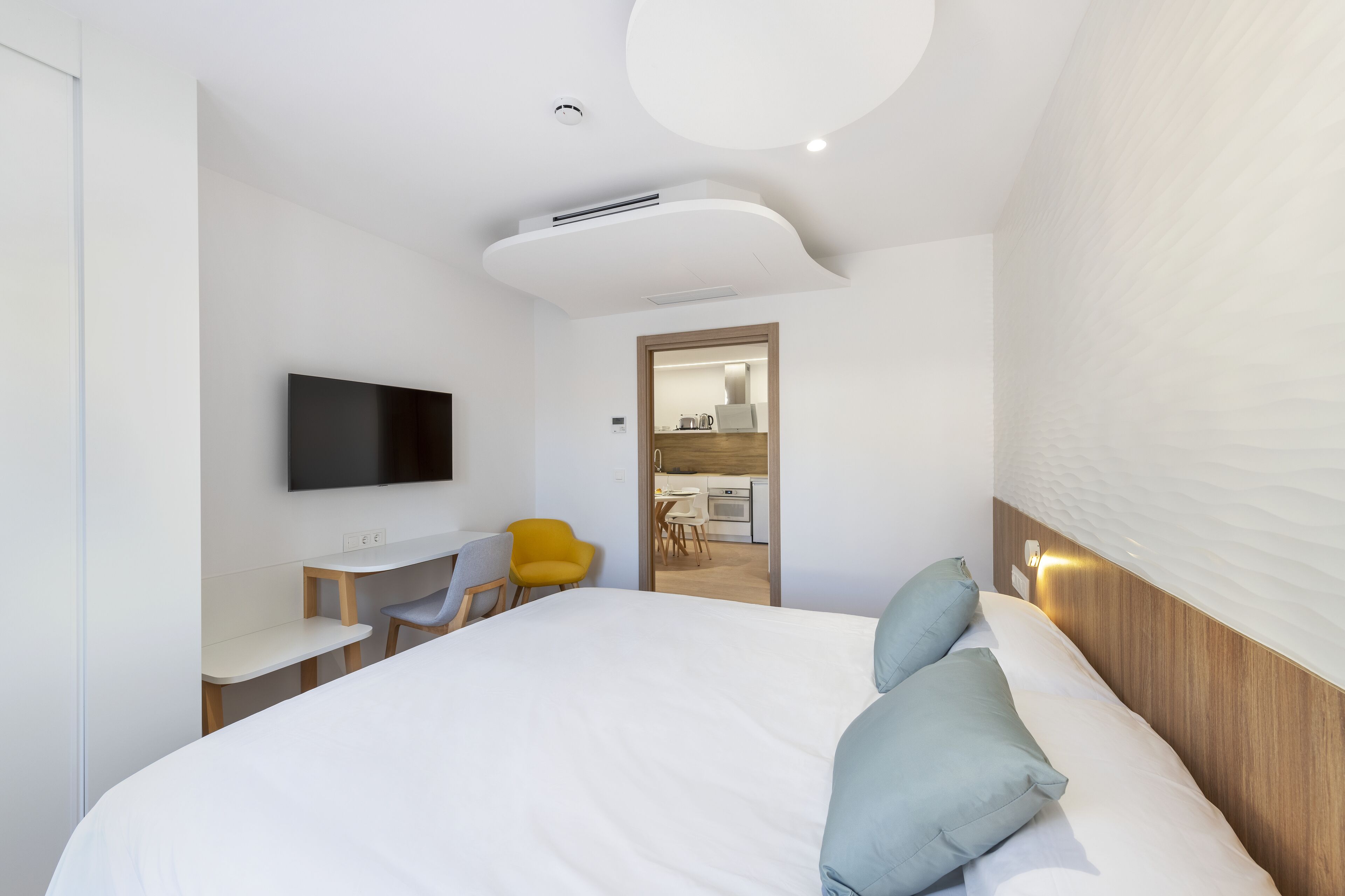 Une chambre d’hôtel moderne, dotée d’un grand lit, d’un téléviseur à écran plat, d’un bureau et d’une chaise jaune vif.