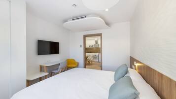 Une chambre d’hôtel moderne, dotée d’un grand lit, d’un téléviseur à écran plat, d’un bureau et d’une chaise jaune vif.
