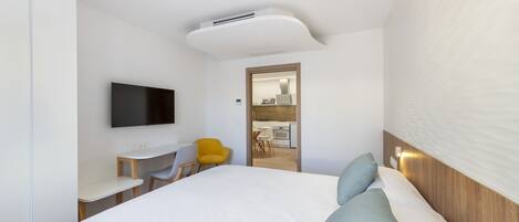 A modern hotel room with a large bed, a flat-screen TV, a desk, and a bright yellow chair.