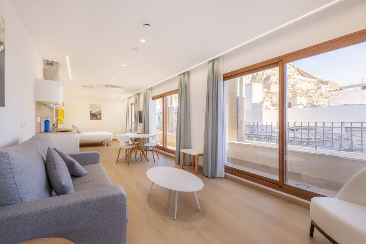 Ein modernes Hotelzimmer mit Balkon, einer Couch, einem Esstisch und einem großen Fenster.