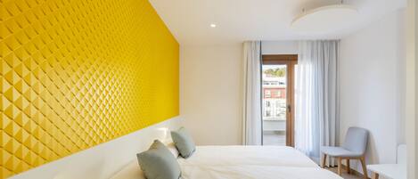 Habitación de hotel con una cama grande, una pared de acento amarillo brillante, un pequeño rincón de estar y vistas al exterior.