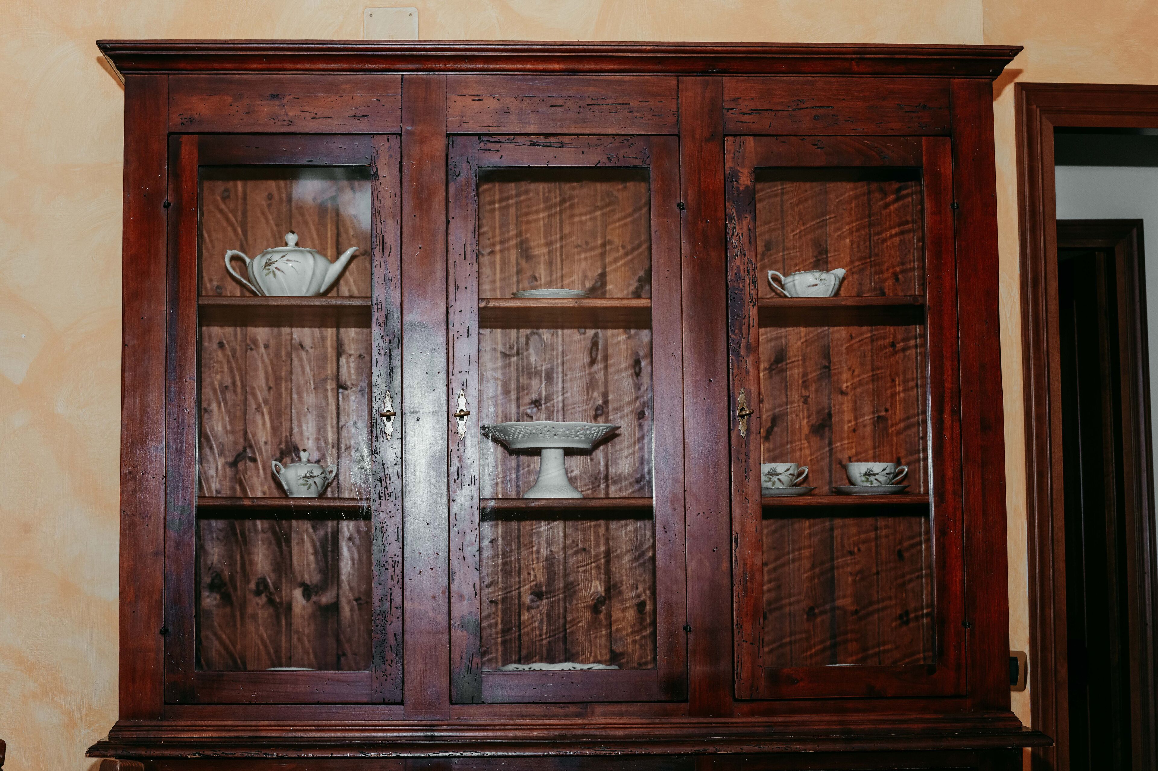 A wooden cabinet with glass doors containing various tea sets.