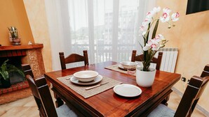 Comedor con mesa de madera, sillas, un florero y vista a través de cortinas translúcidas.