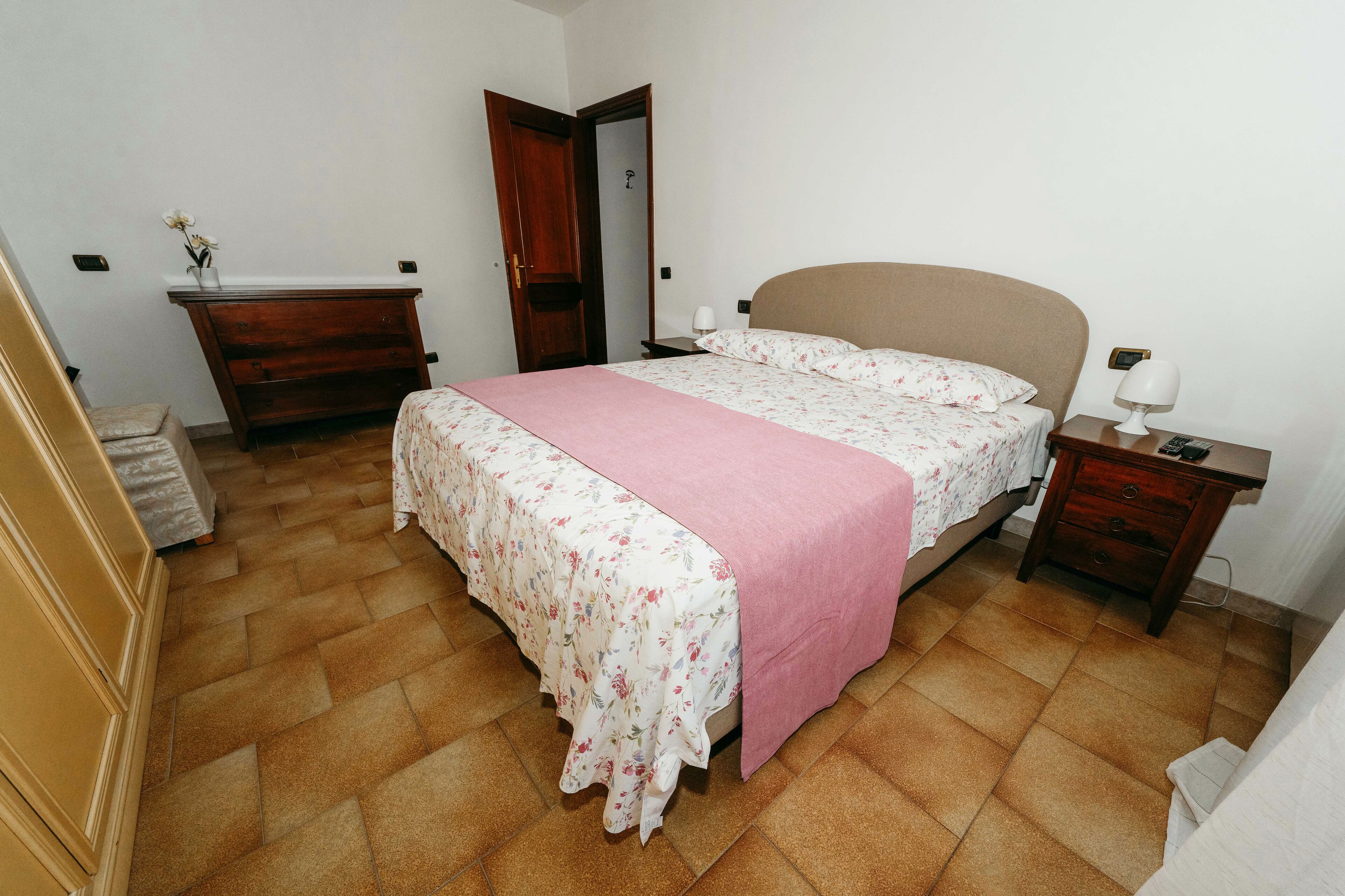 Un dormitorio con cama, mesita de noche, cómoda y una puerta que da a otra habitación.