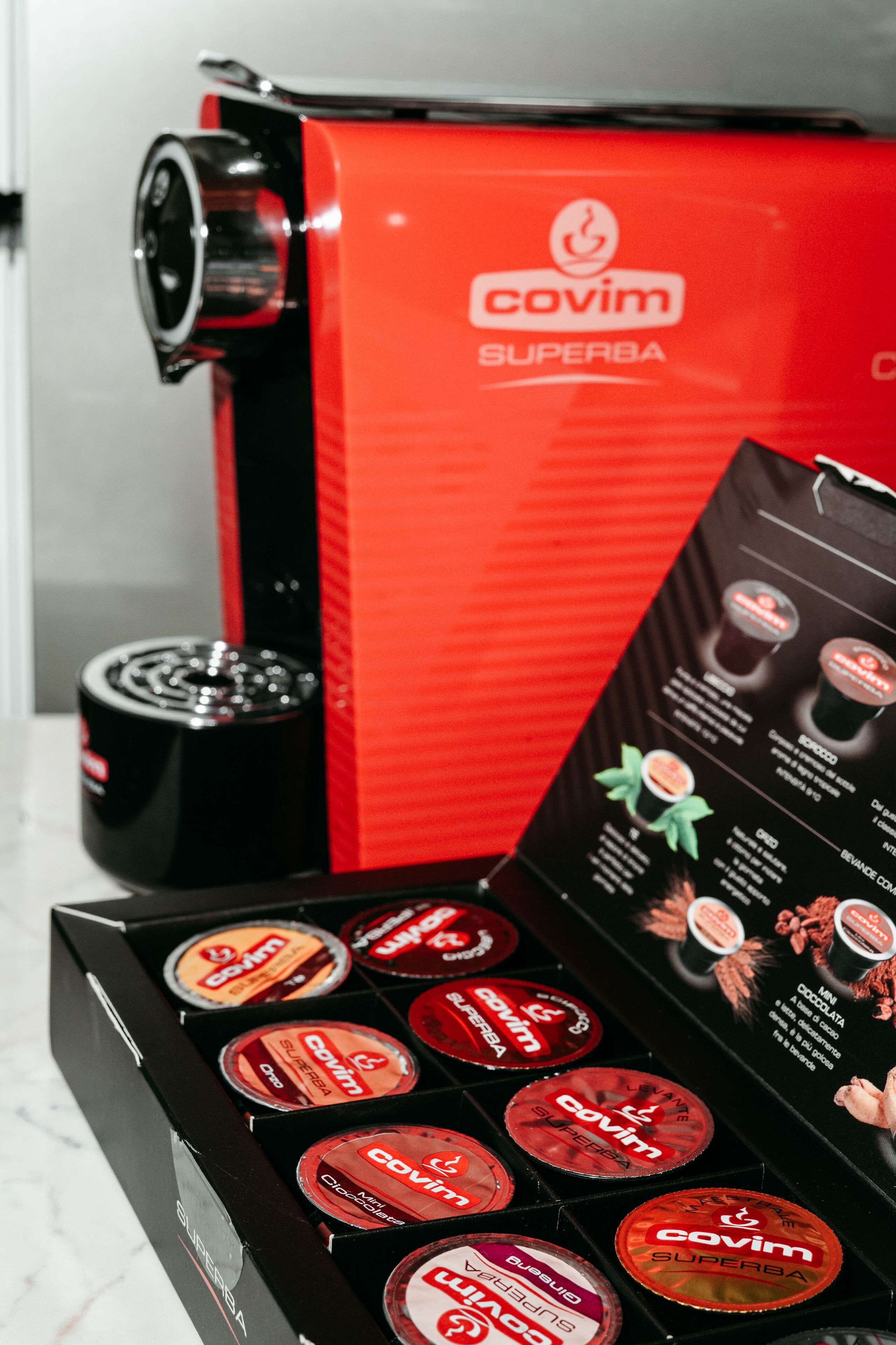Une machine à expresso COVIM SUPERBA rouge, dotée d’un présentoir pour les capsules de café.