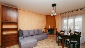 Una sala de estar con sofá modular, aparador de madera, mesa de comedor con sillas y chimenea.
