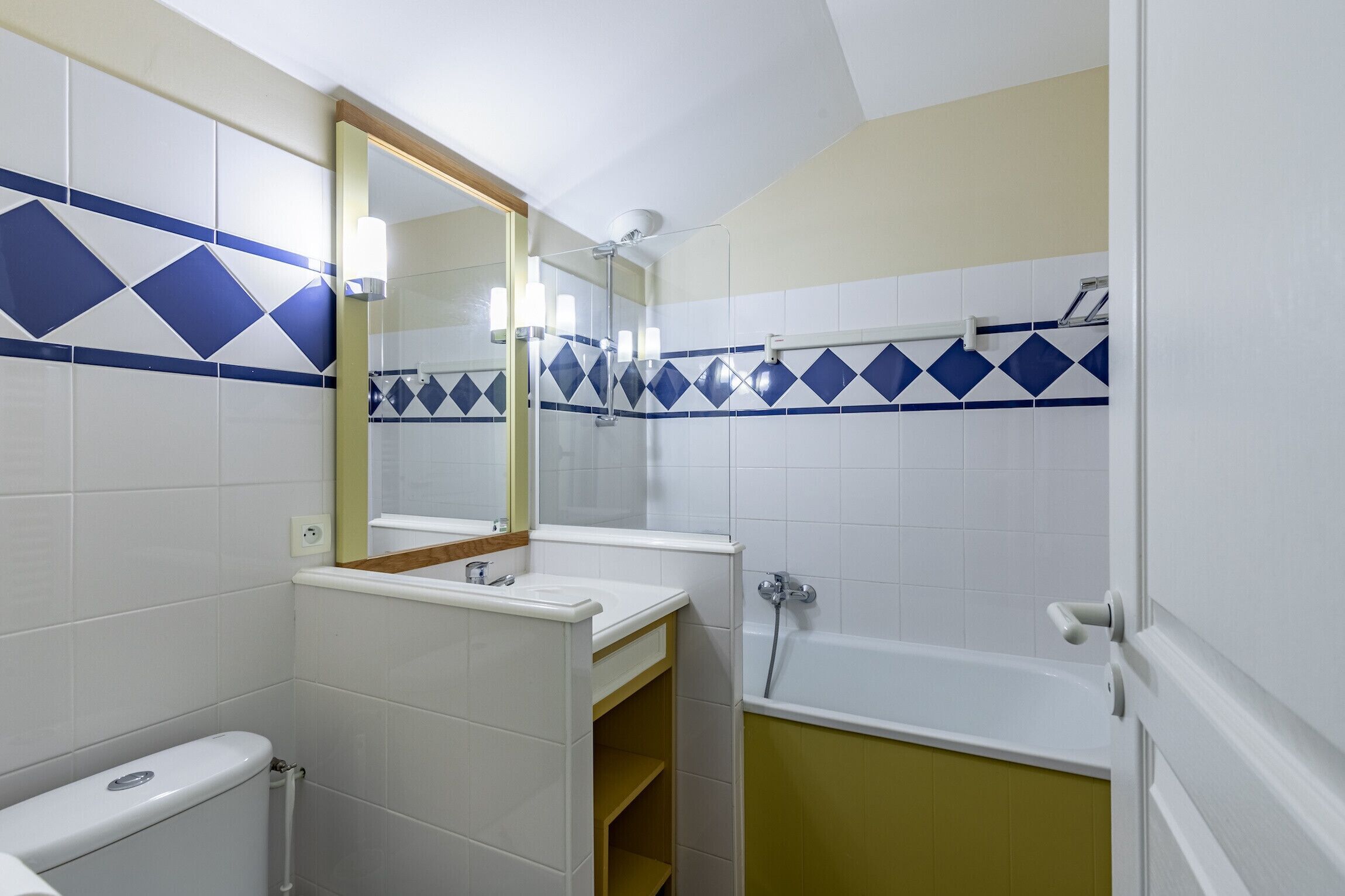 A bathroom with white and blue tiles, a toilet, a sink, a mirror, and a bathtub.