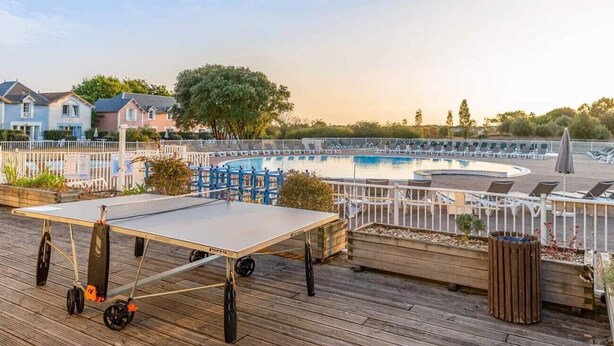 Ein Poolbereich mit Liegestühlen und einem Tischtennis-Tisch auf einer Holzterrasse.