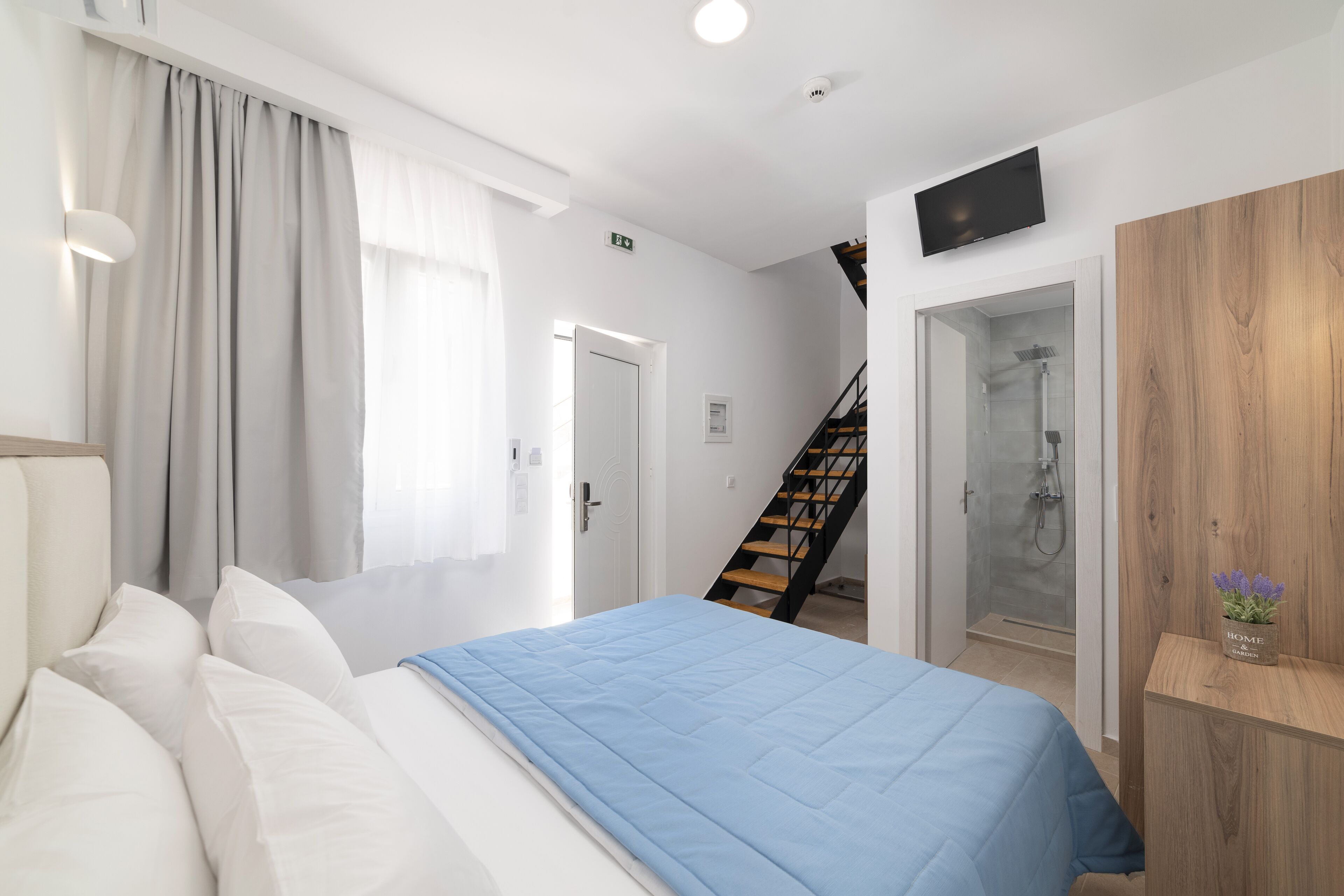 A modern hotel room with a large bed, a wooden wardrobe, a shower area, and a staircase.